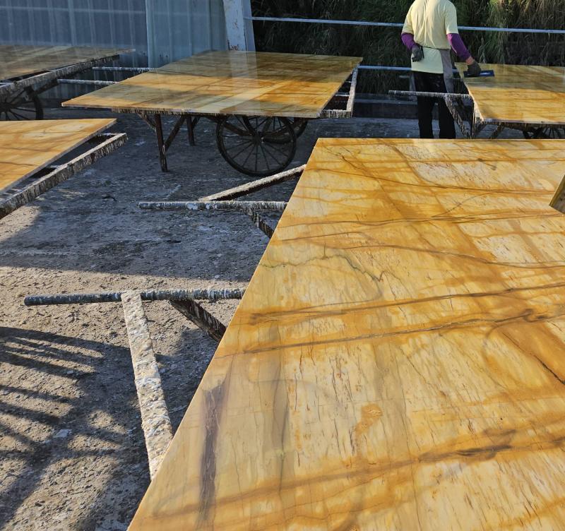 Giallo Siena marble slabs on stands in a workshop, with a worker finishing one by hand